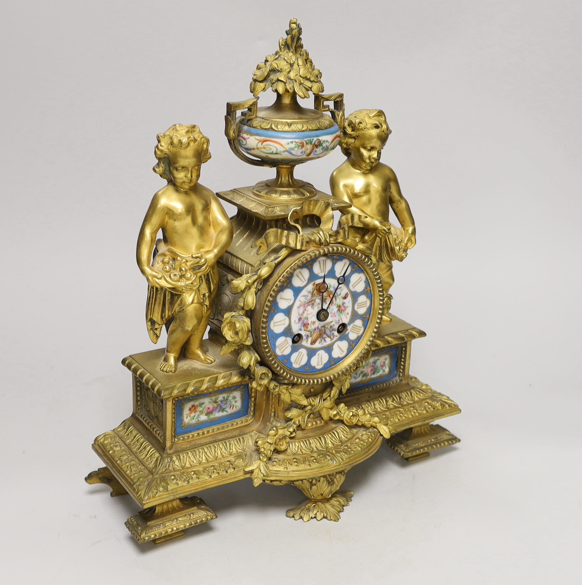 A French decorative ormolu putti mantel clock with porcelain clock face, side panels and urn